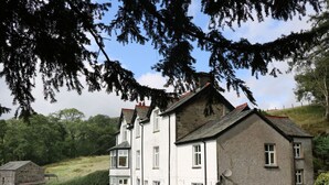 Une maison à deux étages avec une façade en pierre, de nombreuses fenêtres et un grand jardin à l’avant.