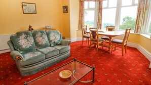 A room with a green sofa, a glass coffee table, a dining table with chairs, and large windows with curtains. - Low Skelgill (Windermere)