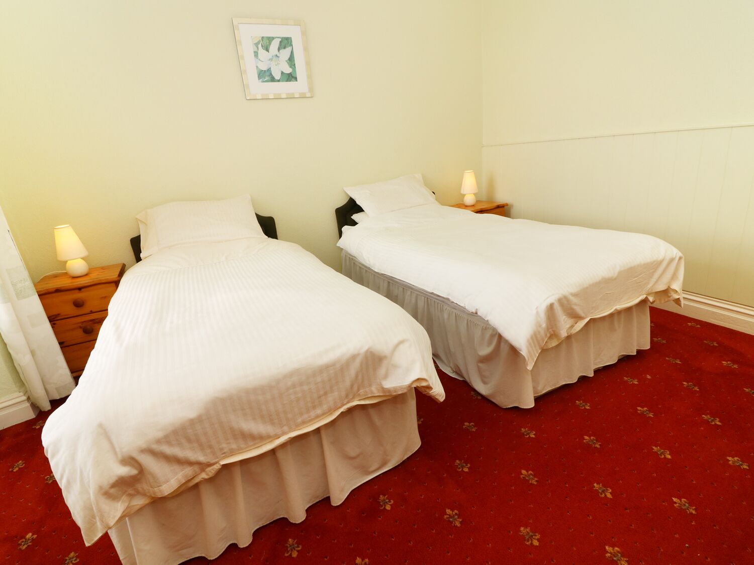 Una habitación con dos camas individuales, cada una con una mesita de noche y una lámpara. La habitación tiene una alfombra roja y un cuadro en la pared.