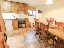 A kitchen with wooden cabinets, a dishwasher, an oven, a microwave, and a dining table with chairs.
