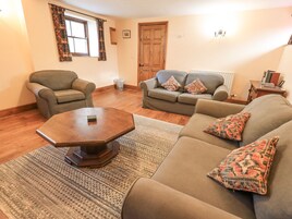 A living room with a sofa, armchair, and coffee table. There is a window with curtains, a door, and a radiator.