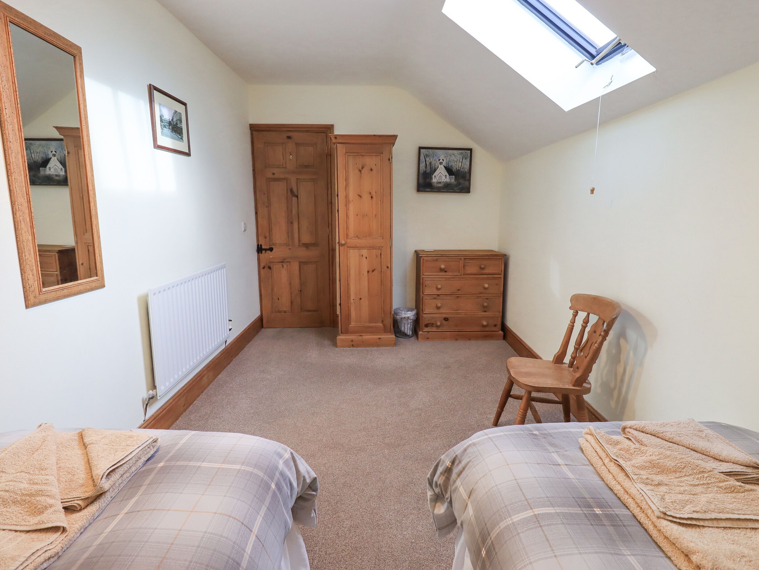 Een slaapkamer met twee bedden, een houten garderobe, een dressoir, een stoel, een radiator en een dakraam.