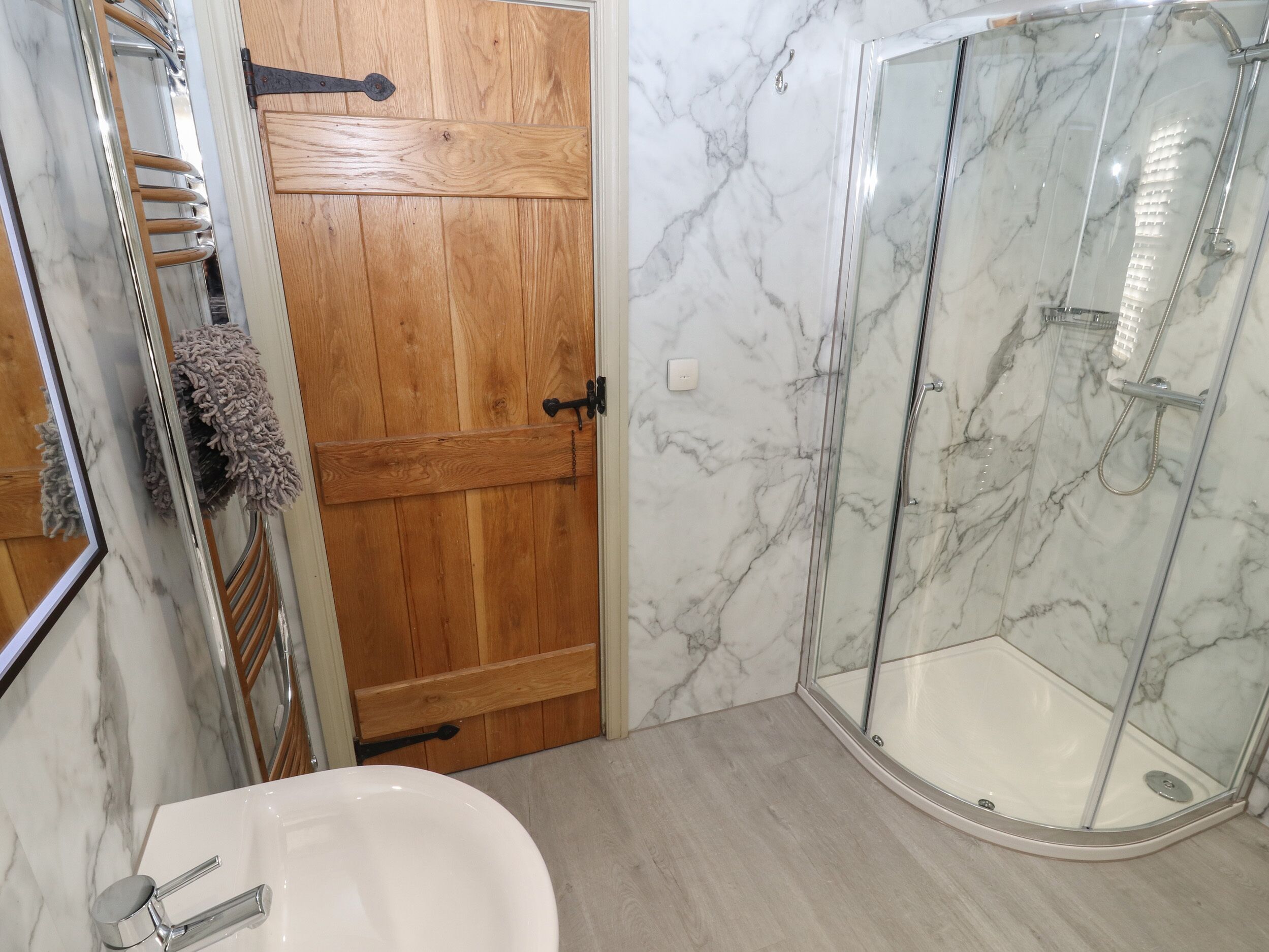 A bathroom with a wooden door, a glass shower enclosure, and a white sink.