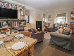 A cozy living room with a fireplace, comfortable seating, a bookshelf, and a dining area set for a meal. - Barney's Cottage (Ambleside)