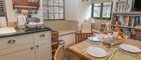 Una cocina acogedora con una mesa de comedor dispuesta para dos, una estantería llena de libros y una ventana con persianas.