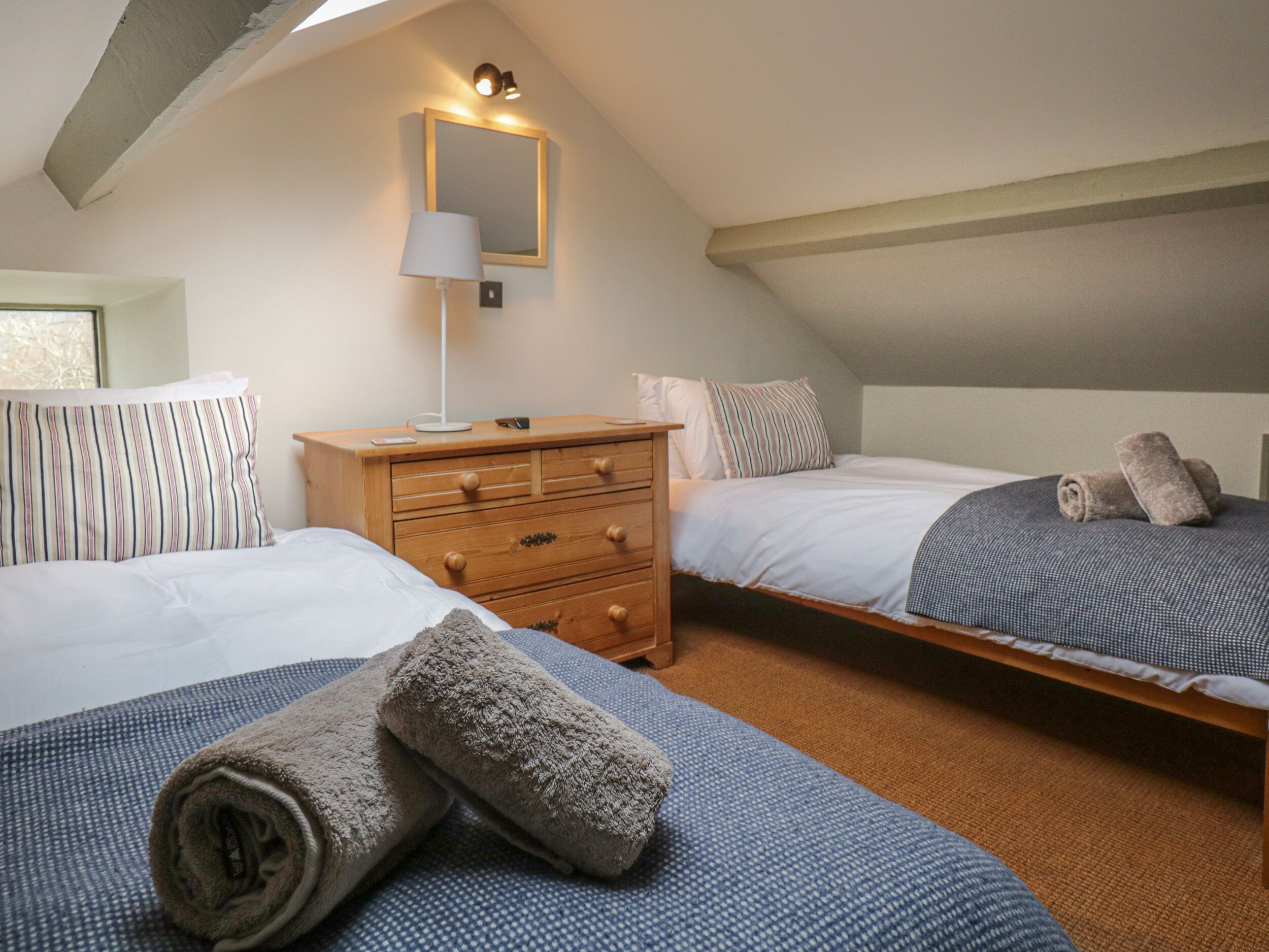 A bedroom with two beds, a wooden dresser, a mirror, and a lamp.