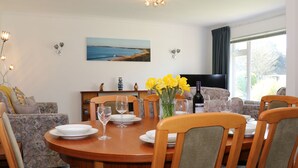 Un coin repas avec une table ronde en bois, dressée pour quatre personnes, entourée de canapés et de fauteuils à motifs.