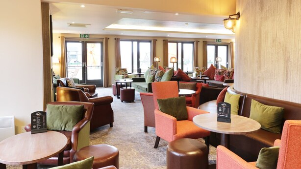 Eine Hotellobby mit mehreren Sitzbereichen, darunter Sofas und Stühle, die um eine zentrale Kaffeebar angeordnet sind.