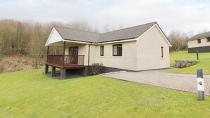 Ein eingeschossiges Haus mit einer Veranda, einem kleinen Garten und einem gepflasterten Auffahrt.