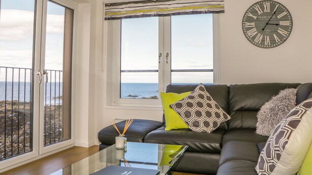 Sala de estar moderna com sofá de couro, mesa de centro de vidro e vista para o mar através de grandes janelas.
