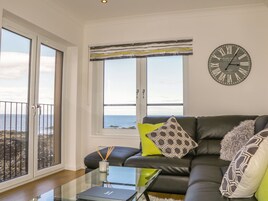 A modern living room with a leather sofa, a glass coffee table, and a view of the sea through large windows.