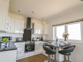 A modern kitchen with white cabinets, a black range hood, a built-in oven, a toaster, and a bar area with two stools.