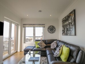A modern living room with a black leather sofa, a glass coffee table, and a cityscape painting.