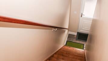 Una escalera estrecha con escalones de madera y barandilla blanca, que lleva a una puerta con panel de vidrio esmerilado.
