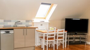 A compact kitchen with a dishwasher, a dining table with chairs, a TV on a stand, and a skylight above the sink. - Providence Apartment (Doncaster)
