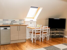 Una cocina funcional con lavavajillas, una mesa de comedor con sillas, un televisor sobre un mueble bajo y un tragaluz sobre el fregadero.