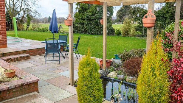 A patio area with a wooden pergola, a small pond, and a seating arrangement with chairs and a table. - Providence Apartment (Doncaster)