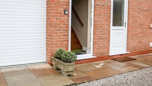 A residential building with a white garage door, a brick exterior, and a small garden area with a potted plant. - Providence Apartment (Doncaster)