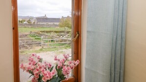 A window with a wooden frame, a curtain, and a vase with pink flowers. - The Old Bakery Barn (Bakewell)