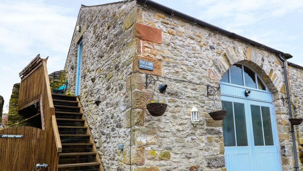 A stone building with a wooden staircase leading to a blue door. - The Old Bakery Barn (Bakewell)