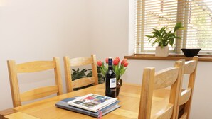Ein Holztisch mit vier Stühlen, einer Weinflasche, einer Vase mit Tulpen und einer Zeitschrift darauf.