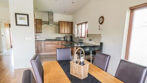 Une cuisine moderne avec des meubles en bois, un plan de travail noir et un coin repas comprenant une table en bois et des chaises en cuir.