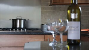 Une cuisine avec un fourneau, une casserole, une bouteille de vin et un verre à vin.