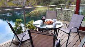 Une terrasse avec une table dressée pour le petit-déjeuner, offrant une vue sur un lac et des collines boisées.