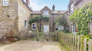 A stone building with a wooden fence, a paved courtyard, and a chimney. - Briar Cottage (Alnwick)