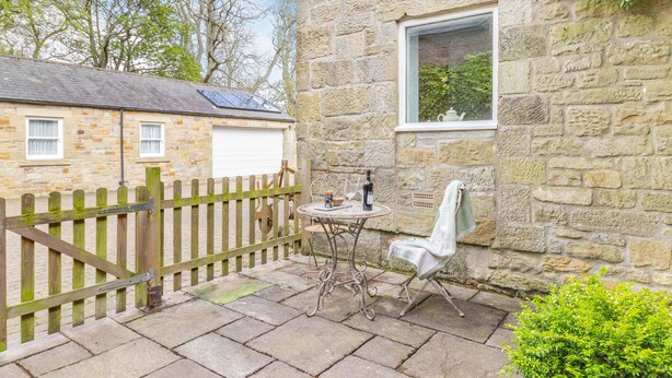 A stone building with a window, a table with a bottle and glasses, and a chair. - Briar Cottage (Alnwick)
