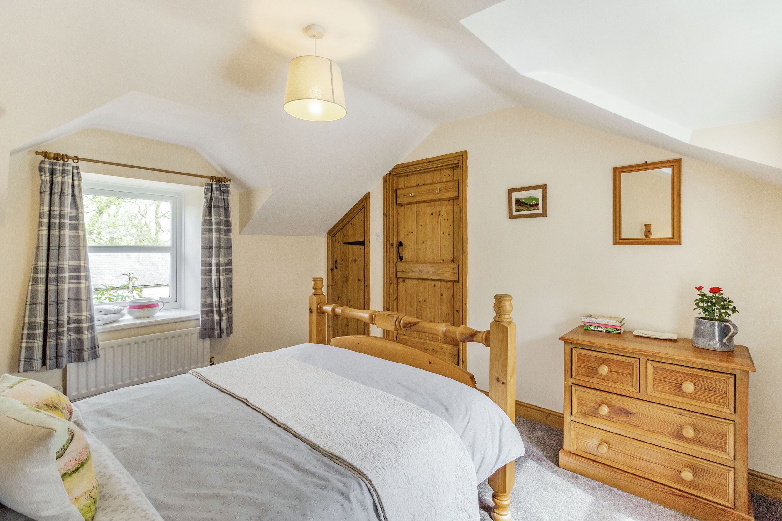 A bedroom with a bed, wooden dresser, and a window with curtains.