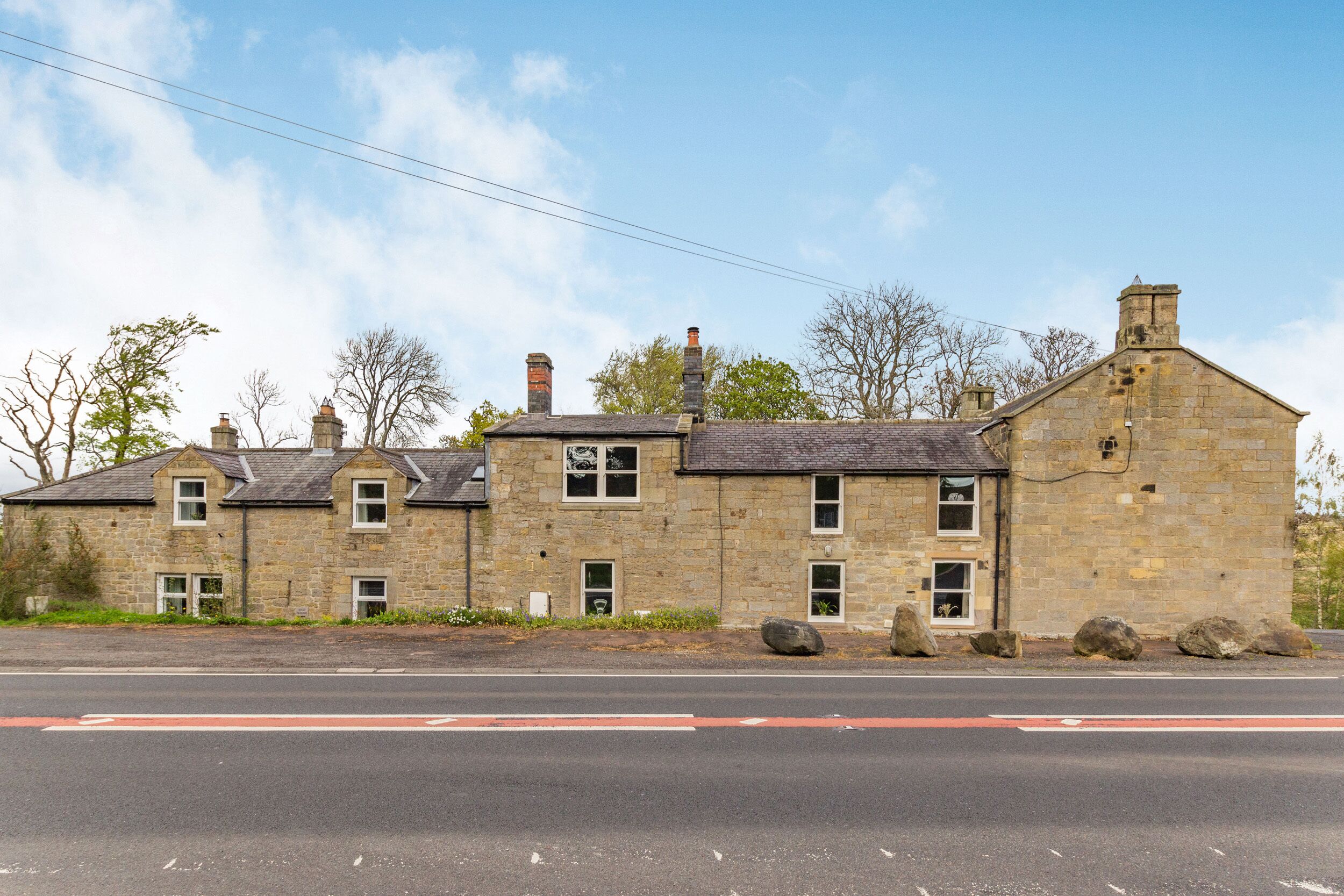 A stone building with multiple chimneys, a paved road in front, and a clear sky.