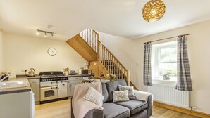 A cozy living room with a grey sofa, wooden staircase, and a kitchen area with modern appliances. - Briar Cottage (Alnwick)