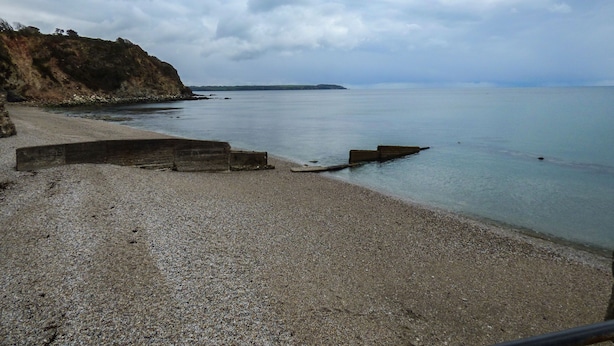 Une plage de galets, avec une falaise rocheuse et une mer calme.