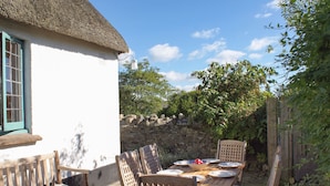 Un espacio de comedor al aire libre de estilo rústico, con un edificio de techo de paja, pared de piedra y muebles de madera.