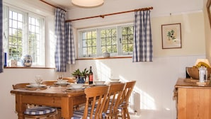 Un comedor con una mesa de madera, sillas y una ventana con cortinas a cuadros.