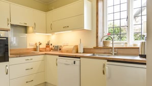 Una cocina moderna con armarios blancos, un lavavajillas Bosch, una encimera de madera y un ventanal con vistas al verdor.