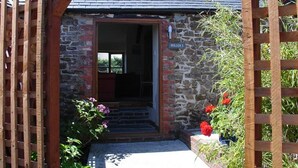 Un bâtiment en pierre avec une porte en bois, une plaque signalétique et un jardin fleuri.