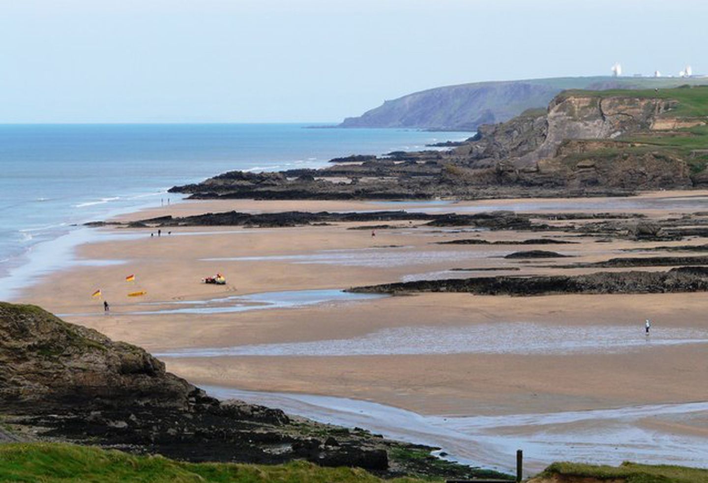 Un paisaje costero con una playa, acantilados rocosos y un faro a lo lejos.