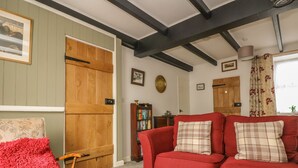 A cozy living room with a red sofa, a wooden bench, and a bookshelf. - Mollys Cottage (Penzance)