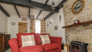 A cozy living room with a red sofa, a stone wall, a wooden fireplace, and a hanging lantern. - Mollys Cottage (Penzance)