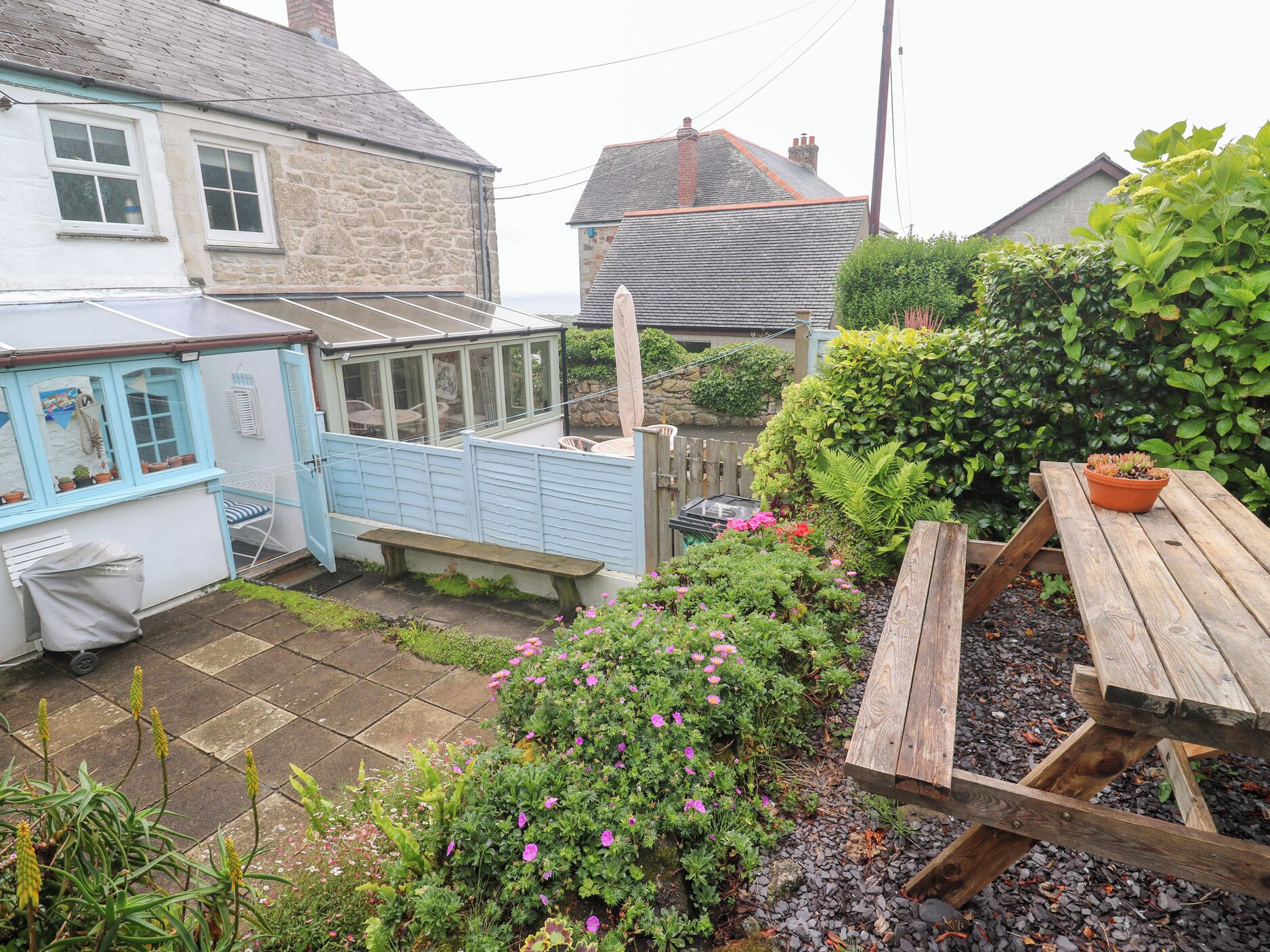 Un espace jardin aménagé avec un banc en bois, une petite table et diverses plantes et fleurs.