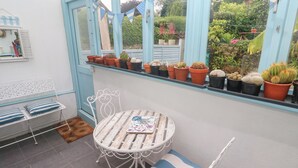 A conservatory with a table and chairs, potted plants, and a view of the garden.