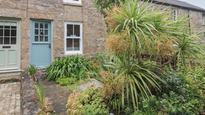 A stone house with a green door and windows, surrounded by lush greenery and plants.