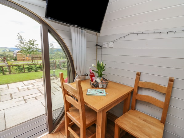 A wooden table with chairs, a potted plant, and a bottle on a balcony with a view of a garden and hills.