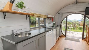 A compact kitchen with a sink, countertop, and cabinets, a window overlooking a garden, and a door leading to an outdoor patio.