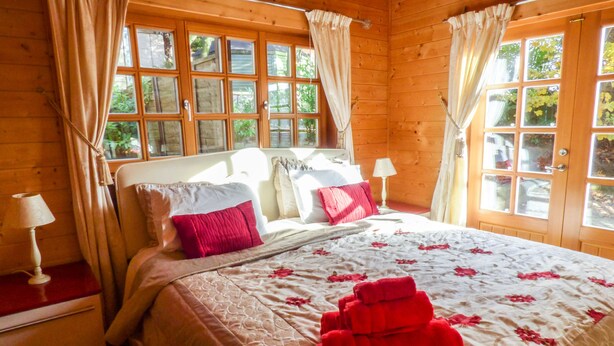 A wooden cabin bedroom with a bed, curtains, and a window. - St Hilda's Lodge (Saltburn-by-the-Sea)
