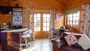 A cozy cabin interior with a wooden ceiling, a bar area, a seating area with a couch, and a dining table. - St Hilda's Lodge (Saltburn-by-the-Sea)