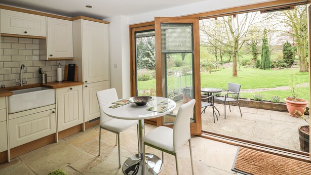 A modern kitchen with white cabinets, a built-in oven, and a dining area with a round table and chairs. - Riverside Lodge (Mansfield)