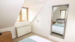 Un dormitorio con techo inclinado, un espejo grande, una cama con colcha azul, un aparador de madera y un radiador.